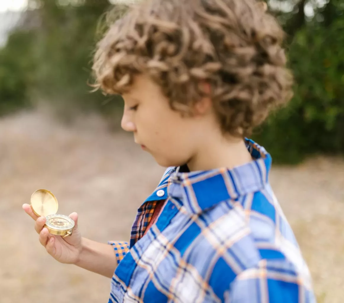 A young boy examines a vintage compass outdoors, showcasing exploration and curiosity.