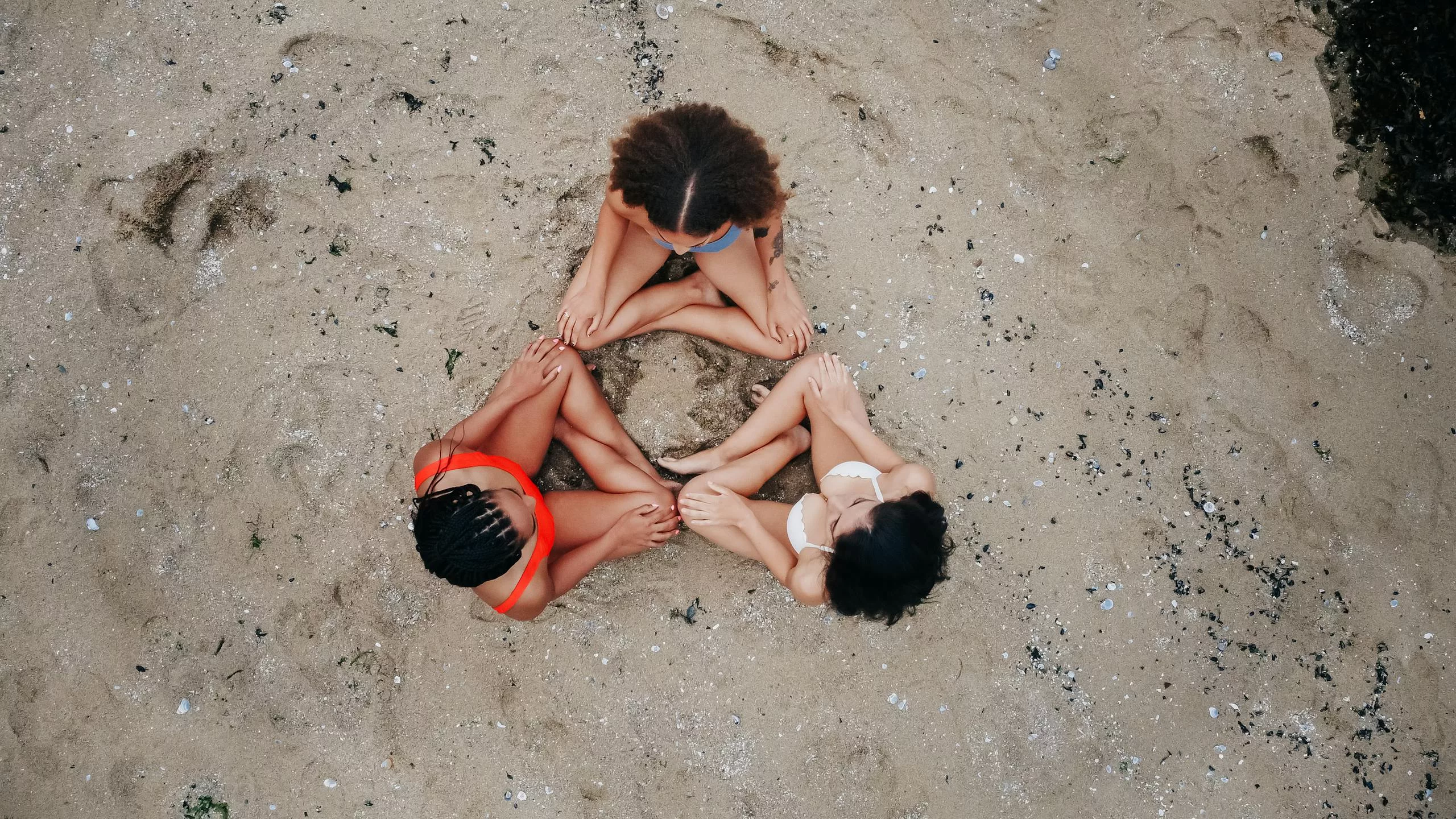 Aerial image of three friends sitting in a circle on a sandy beach in Vancouver, Canada.