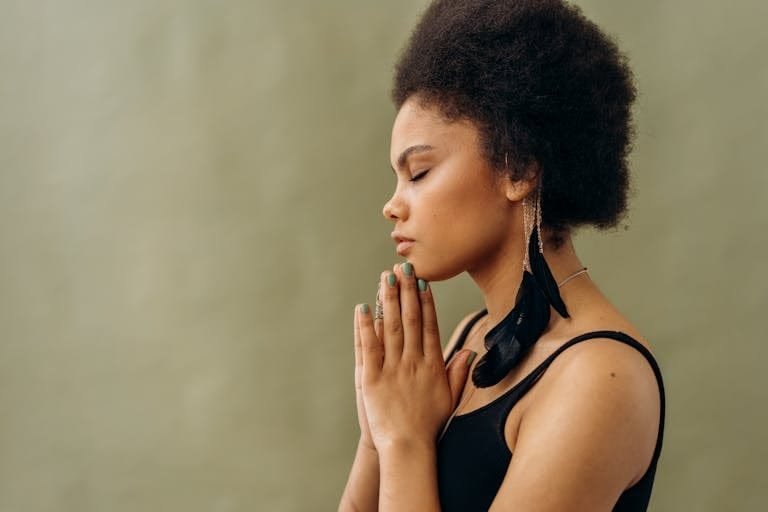 A young woman with afro hair practicing calming meditation indoors. Braeth