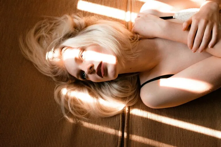 Vrouw ligt op de grond in het zonlicht, haar blik zacht en afwezig; een moment van stilte na pijn of vermoeidheid, symbool voor vallen en weer opstaan bij fibromyalgie. Foto: Camila Cordeiro