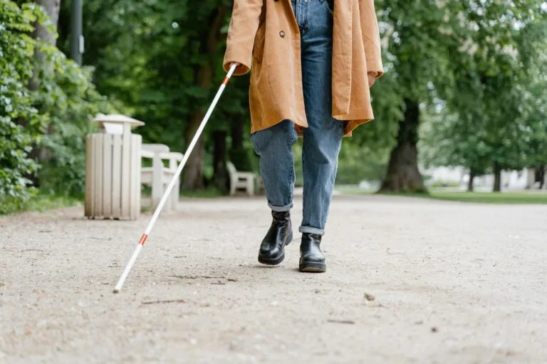 Een vrouw met een witte stok wandelt over straat — symbool voor zelfstandigheid, vertrouwen en de kracht van echt zien.” foto: MART PRODUCTION