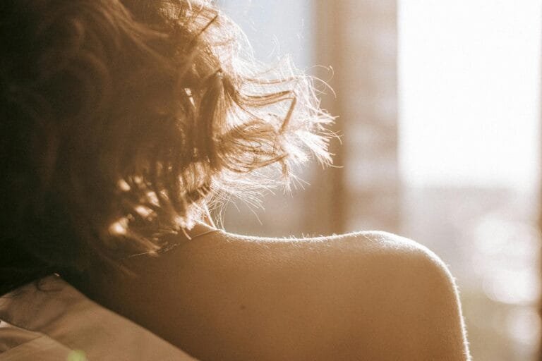 Zachte close up van een schouder in warm ochtendlicht, met licht dat door het haar valt en een intiem moment van stilte suggereert. foto: Marina Ryazantseva