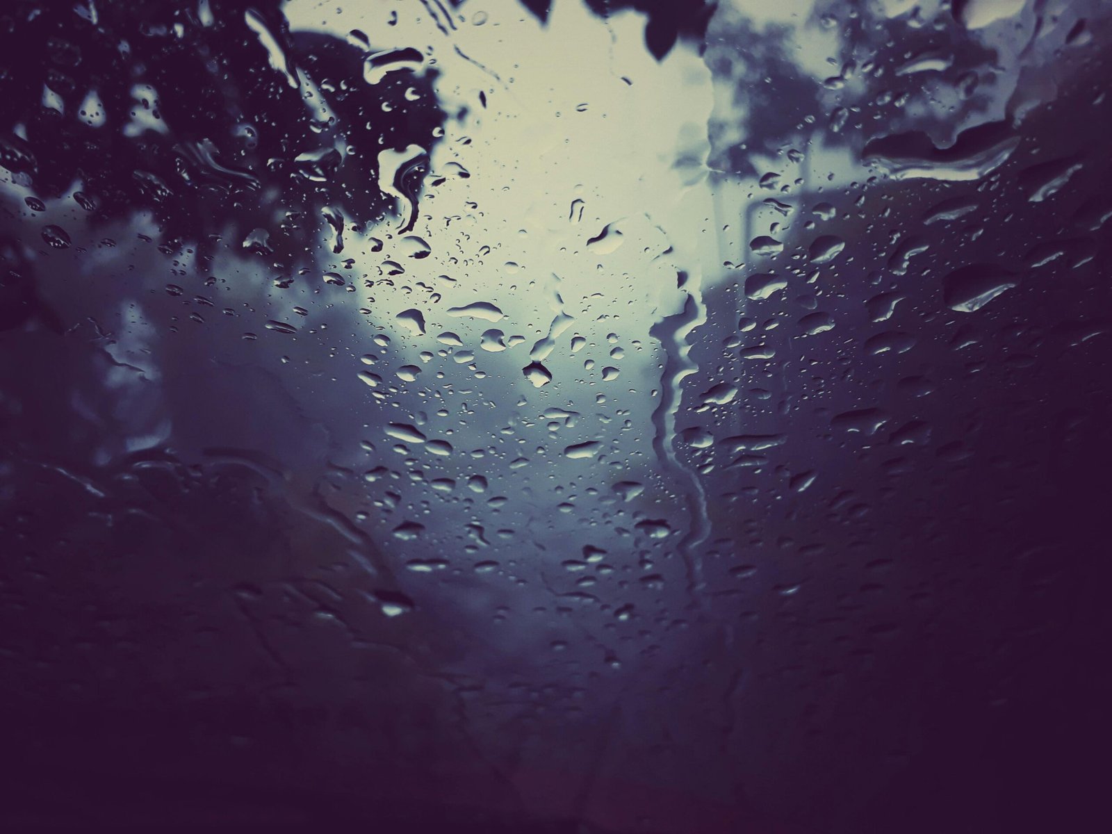 Regendruppels op een raam met een wazige buitenwereld daarachter, een stille grens tussen binnen en buiten die verwerking en integratie suggereert. foto: Ruatsanga hmar
