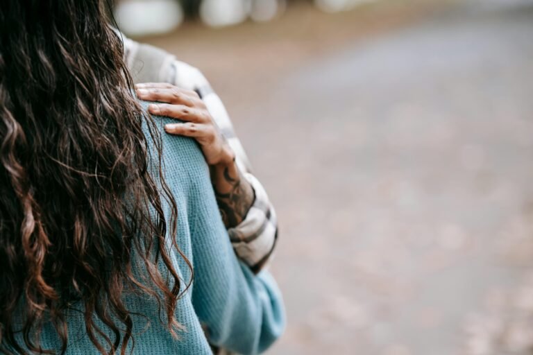 Zachte foto van een persoon van achteren, met een hand die rust op de schouder, symbool voor kwetsbaarheid, nabijheid en het verlangen om geloofd te worden bij onzichtbare ziekte. foto: Tim Samuel