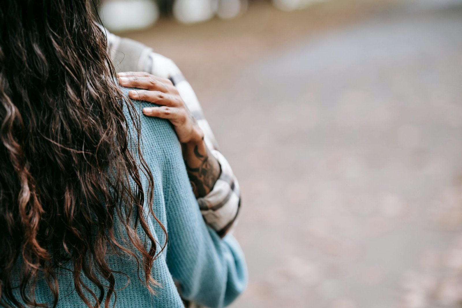 Zachte foto van een persoon van achteren, met een hand die rust op de schouder, symbool voor kwetsbaarheid, nabijheid en het verlangen om geloofd te worden bij onzichtbare ziekte. foto: Tim Samuel