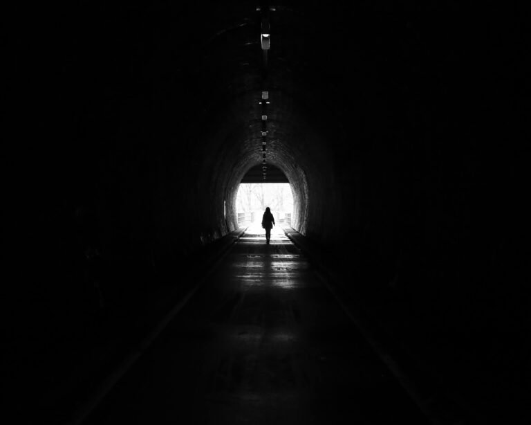 Silhouet van een vrouw die door een donkere tunnel loopt naar fel daglicht, als symbool voor heling en het terugkeren naar een plek die ooit overweldigend voelde. foto: Mika Lika