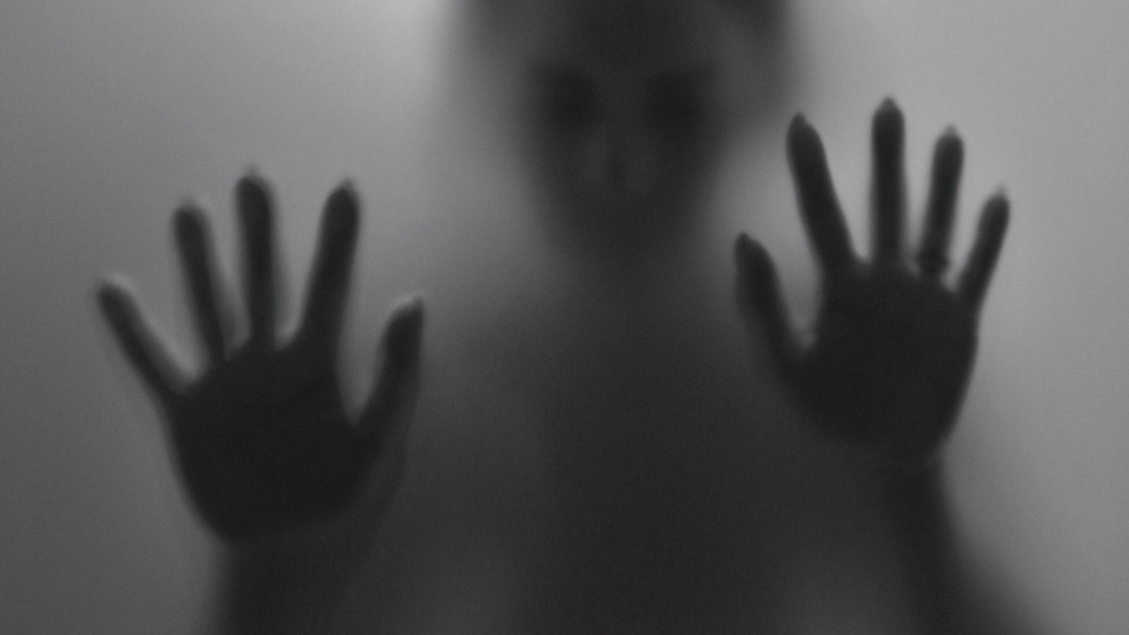 Silhouet van een persoon achter matglas met handen tegen het oppervlak, symbool voor innerlijke spanning en een lichaam dat alarm slaat zonder zichtbare oorzaak. foto: Wunderbilder