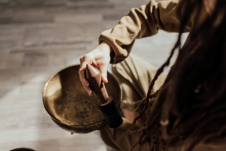 Hand die een klankschaal aanslaat tijdens een soundhealing sessie in een rustige ruimte met zacht licht foto: Arina Krasnikova