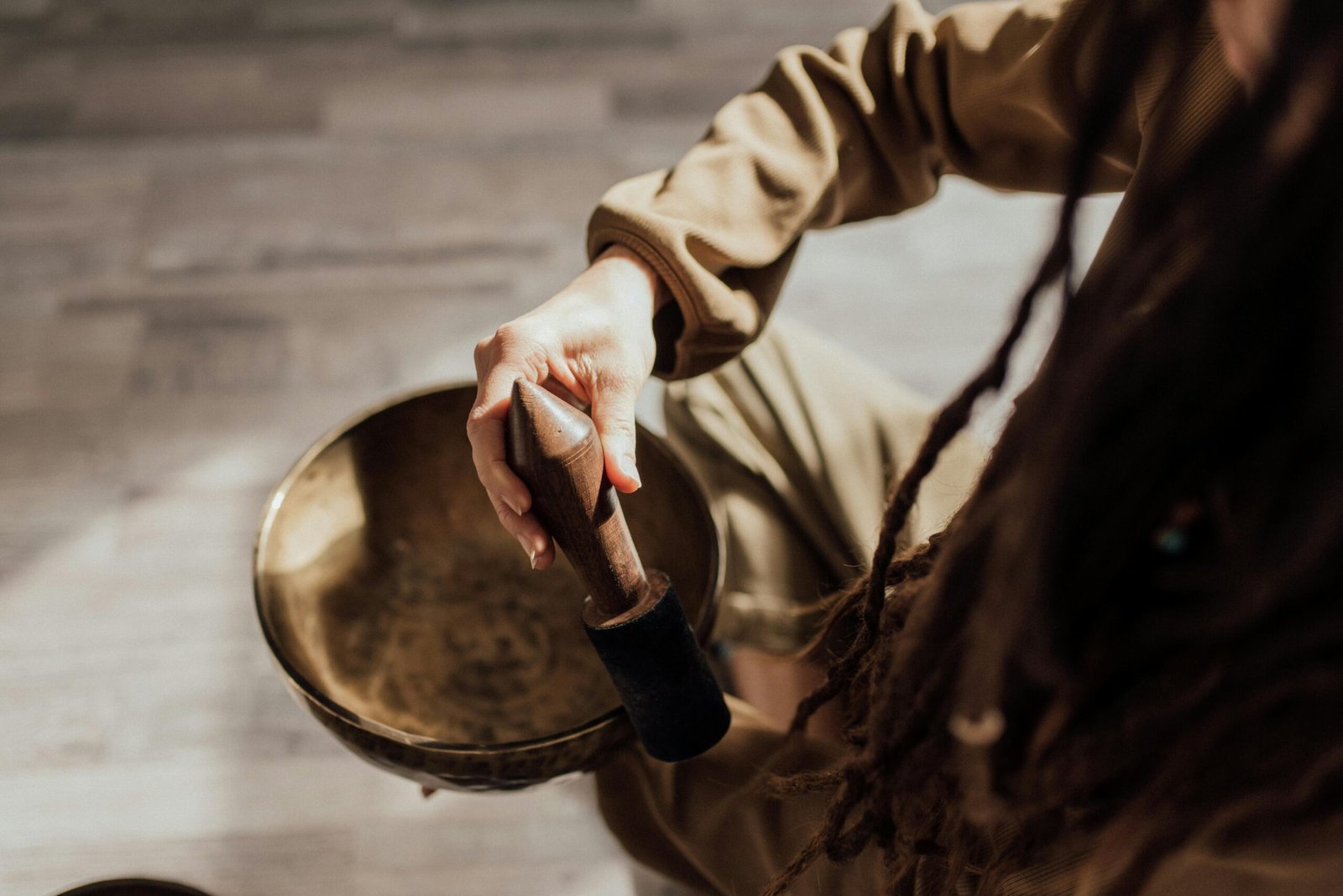 Hand die een klankschaal aanslaat tijdens een soundhealing sessie in een rustige ruimte met zacht licht foto: Arina Krasnikova