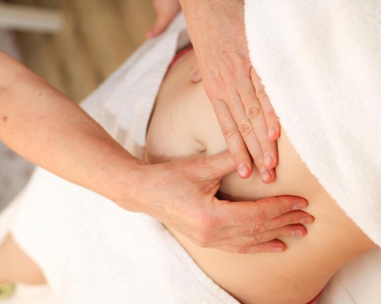Twee handen die een zachte buikmassage geven op een ontspannen lichaam, bedekt met witte handdoeken, tijdens een Chi Nei Tsang sessie. foto: Lara Stratychuk