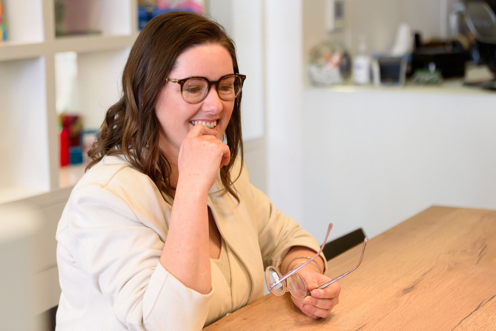 Lachende vrouw met schildpadkleurige bril in optiekwinkel Jeline Wijnegem, houdt een tweede montuur vast aan tafelfotograaf: MArvin Anthony
